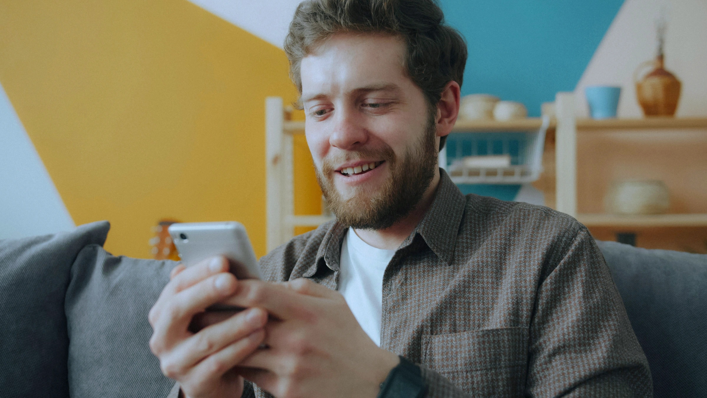 Un homme sourit en regardant son téléphone sur un canapé